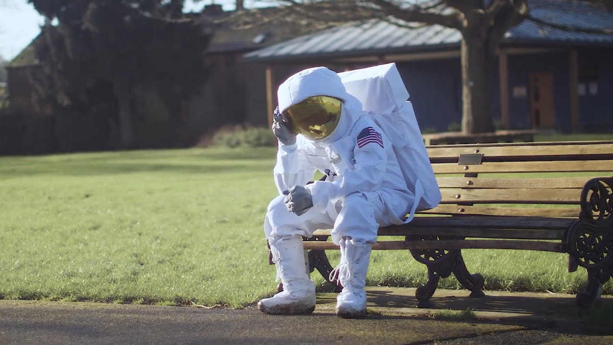 Un homme déguisé en astronaute assis sur un banc public dans un parc