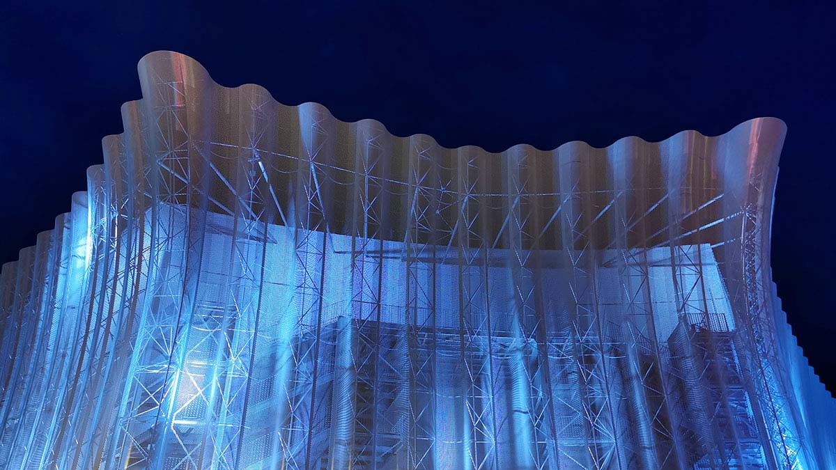 Vue nocturne d'une façade de bâtiment à l'architecture ondulée illuminée en bleu