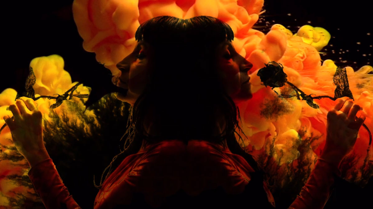 Silhouette d’une femme de profil en double exposition, bras levés tenant des roses fanées, devant des nuages d’encre orange sur fond noir