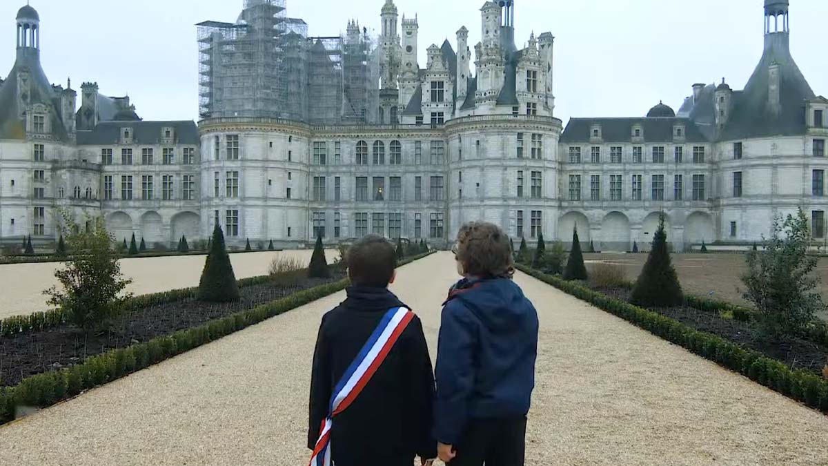 Deux enfants de dos, dont un avec écharpe tricolore, face au Château de Chambord